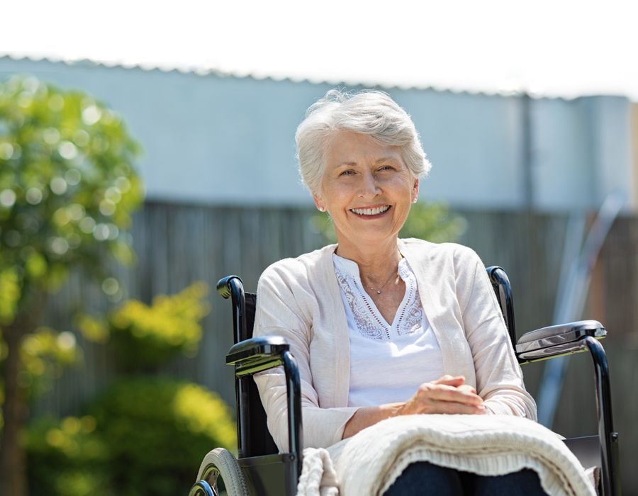 Older woman sitting outside in her wheelchair smiling at the camera