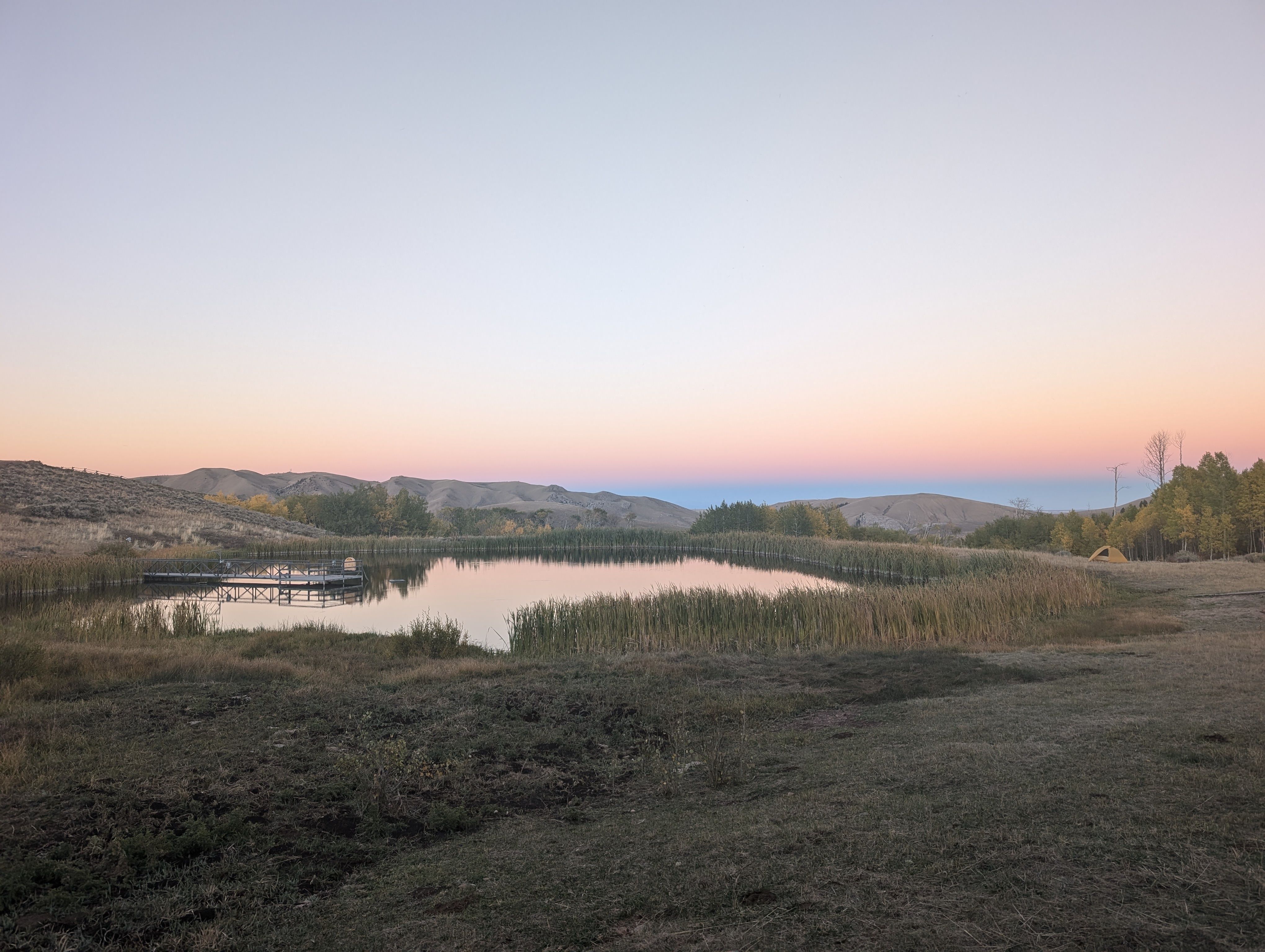 A view of a pond surrounded by grass, with a sunset in the distance