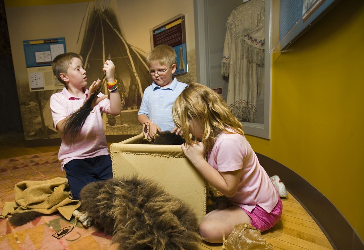 two boys and a girl playing in a box of buffalo items at the Smoky Hill Museum.