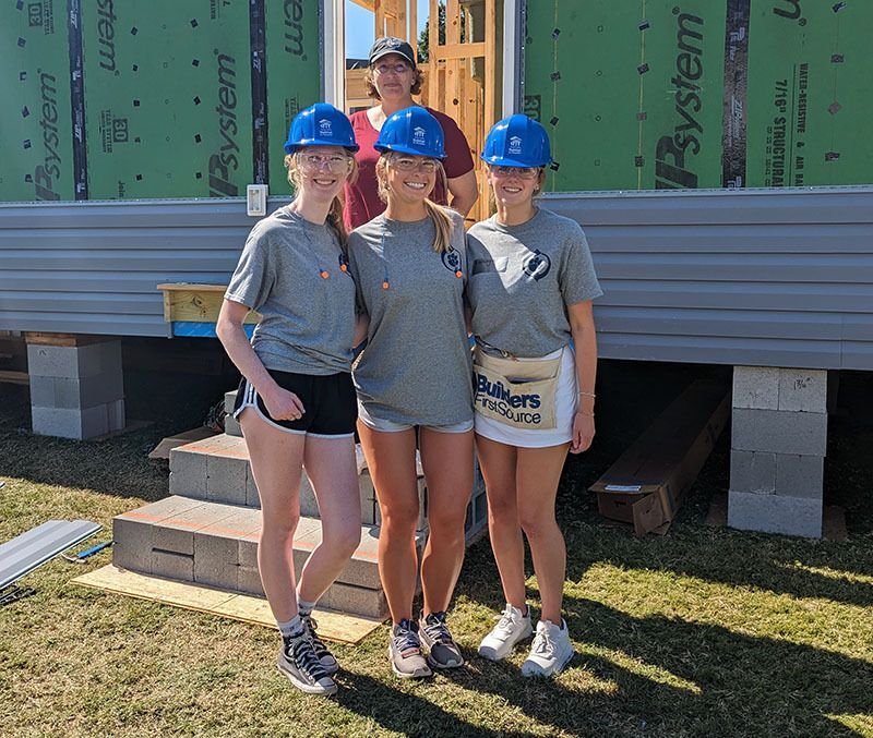 A group of young women stand in front of a home under construction. 