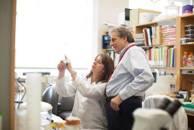 A female scientist, sitting, holds up a paper and points, while a male scientist stands behind her looking at the paper.