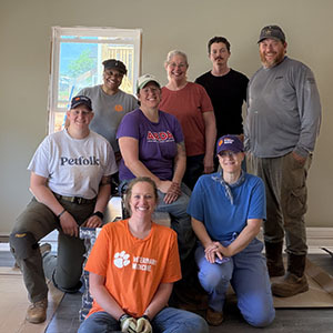 Group of volunteers in Clemson Veterinary Medicine and other team shirts posing together inside a home under renovation