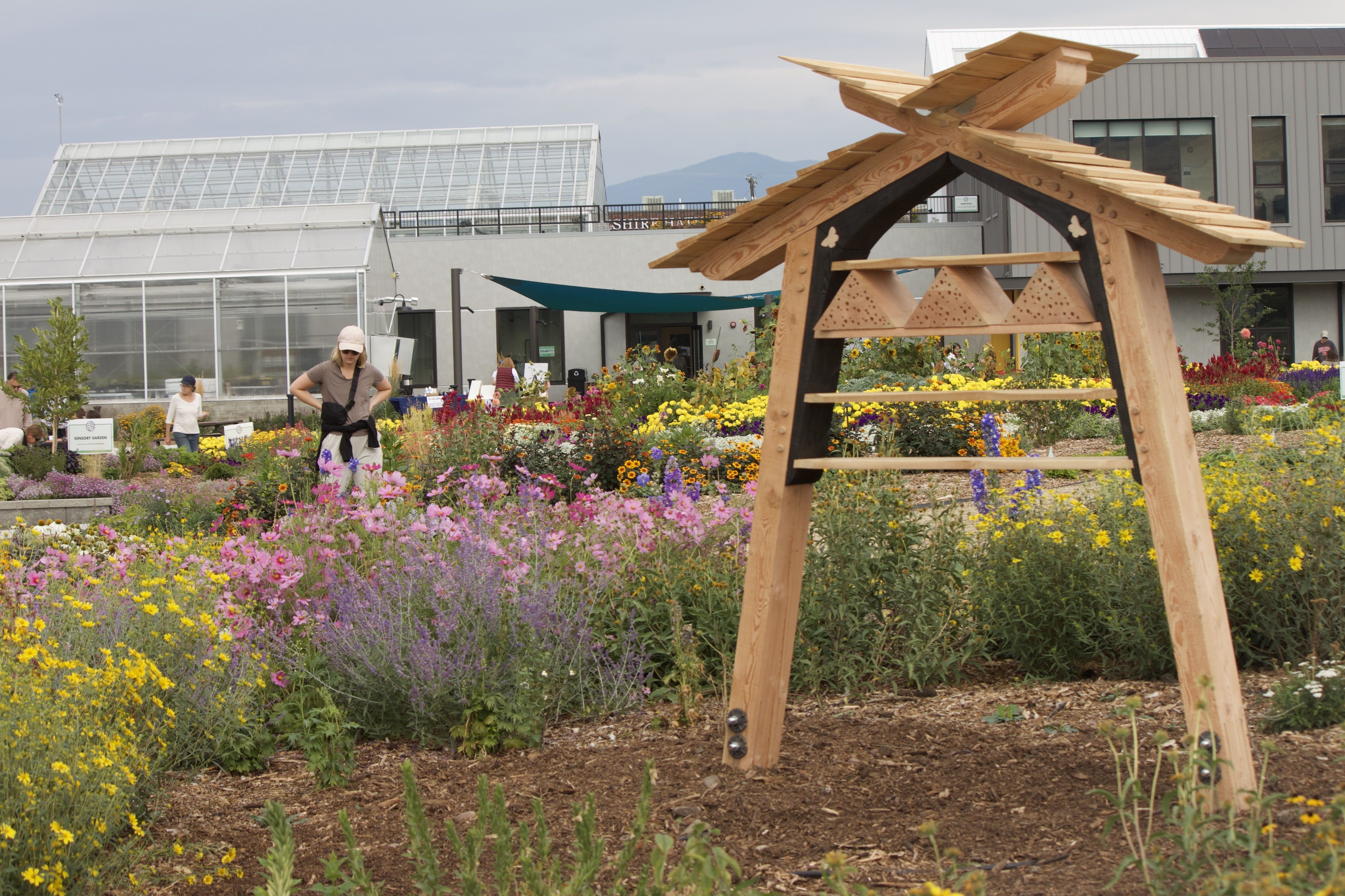 Garden with pollinator structure and greenhouse in the background.