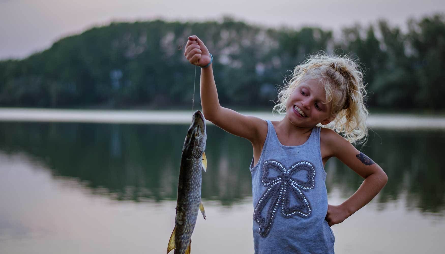 Girl smiling at the fish she is holding.