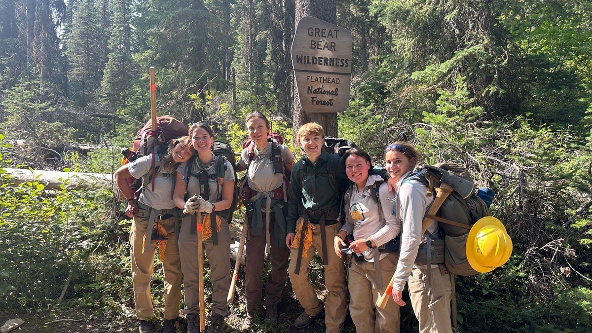 [Image Description: A crew stands smiling in front of a Wilderness sign, holding tools and ready to head into the backcountry.]