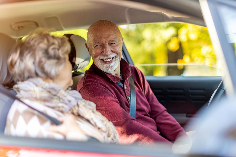 Older male driver looks toward his female passenger.