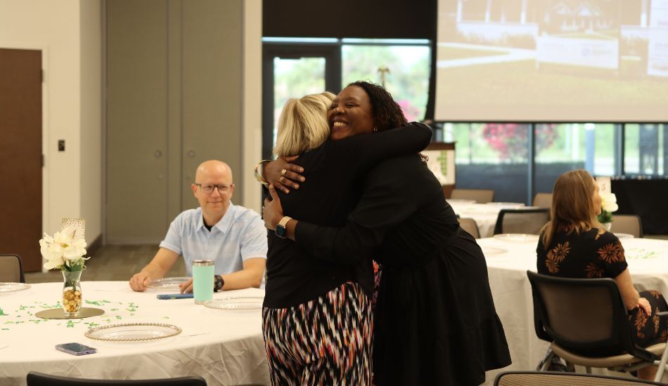 Photo of executive director Monifa Watson hugging a donor and smiling widely, at a "thank you" brunch for donors and partners.