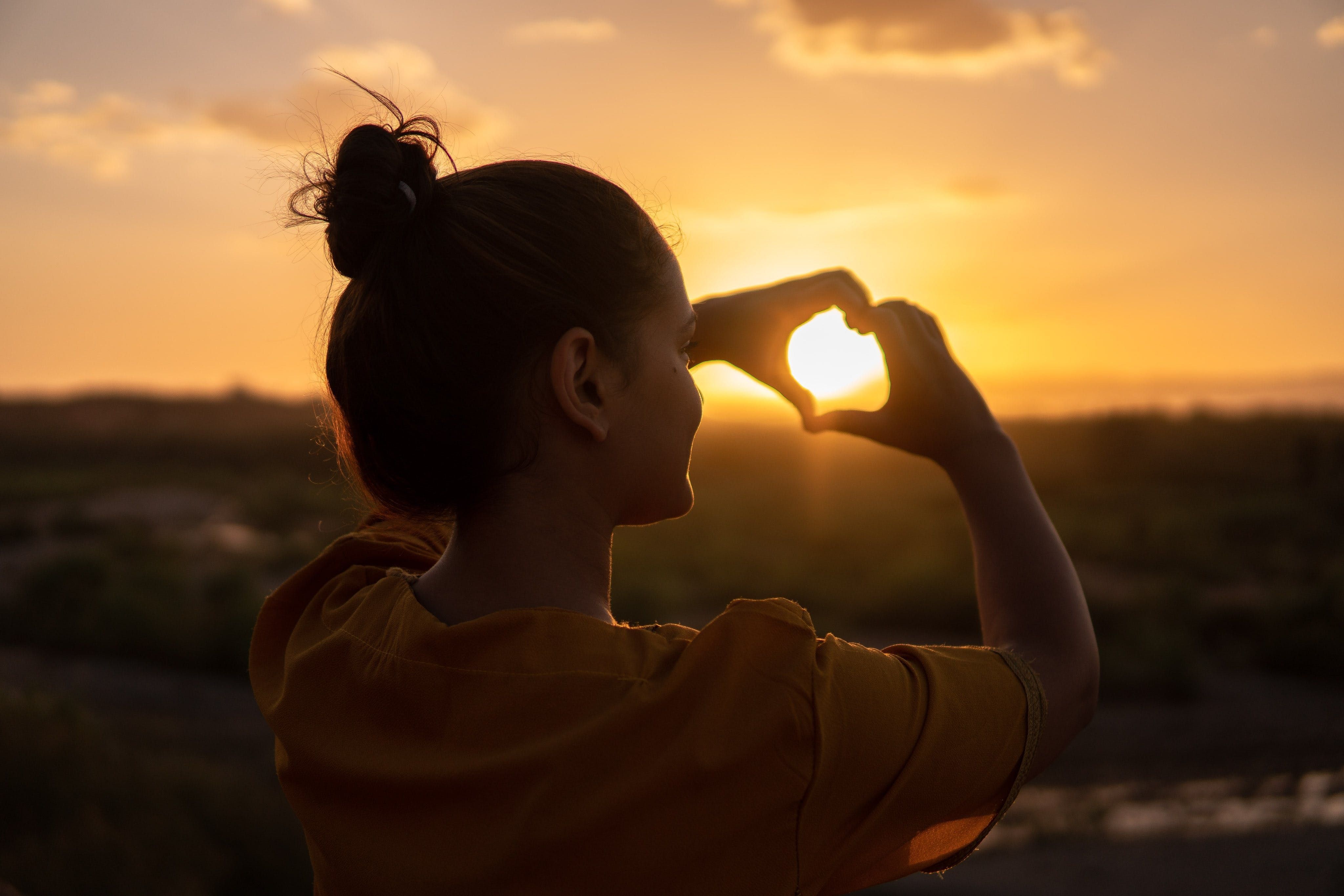 woman in sunset making heart shape with hands