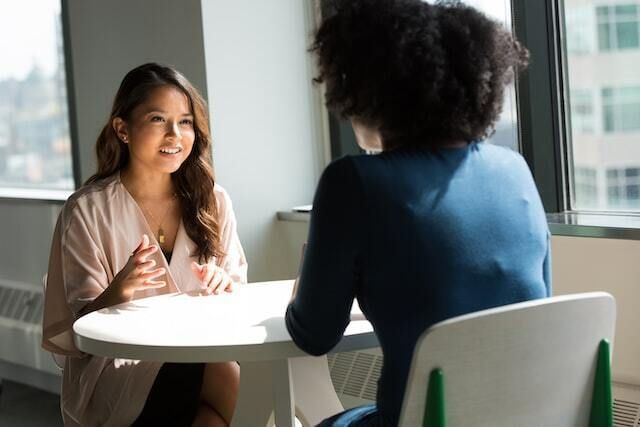 Two women sitting at a white table talking