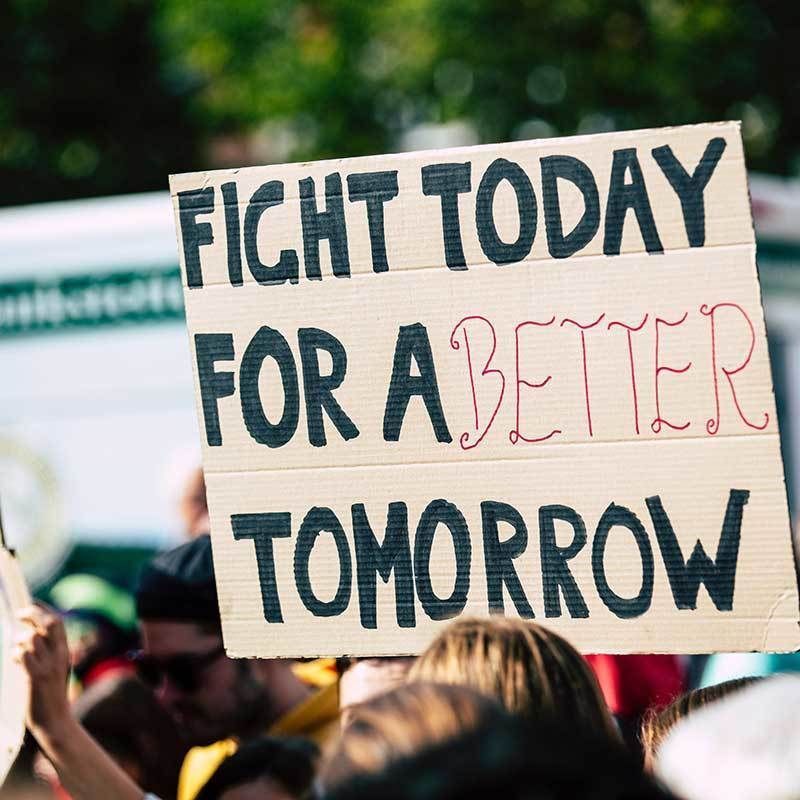 A cardboard sign above a group of people that reads: Fight today for a better tomorrow.
