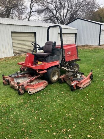 image of a red riding lawn mower on green grass in front of a white shed
