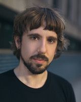 Nick Walther. A man who has a lot of facial hair and a grim look on his face. He is posing for his headshot.