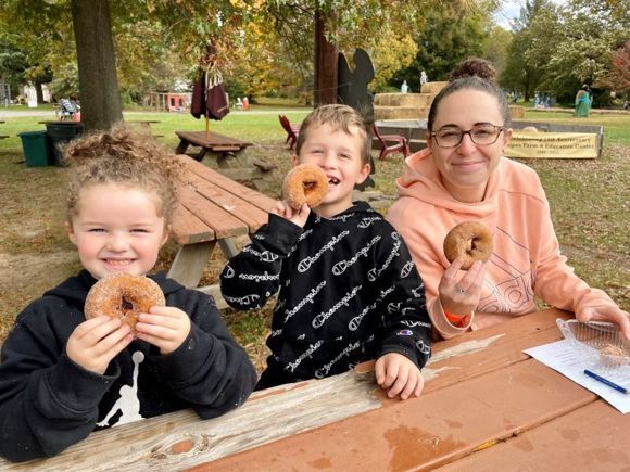 A mother and her two young children enjoy fresh baked cider donuts at Snipes Farm