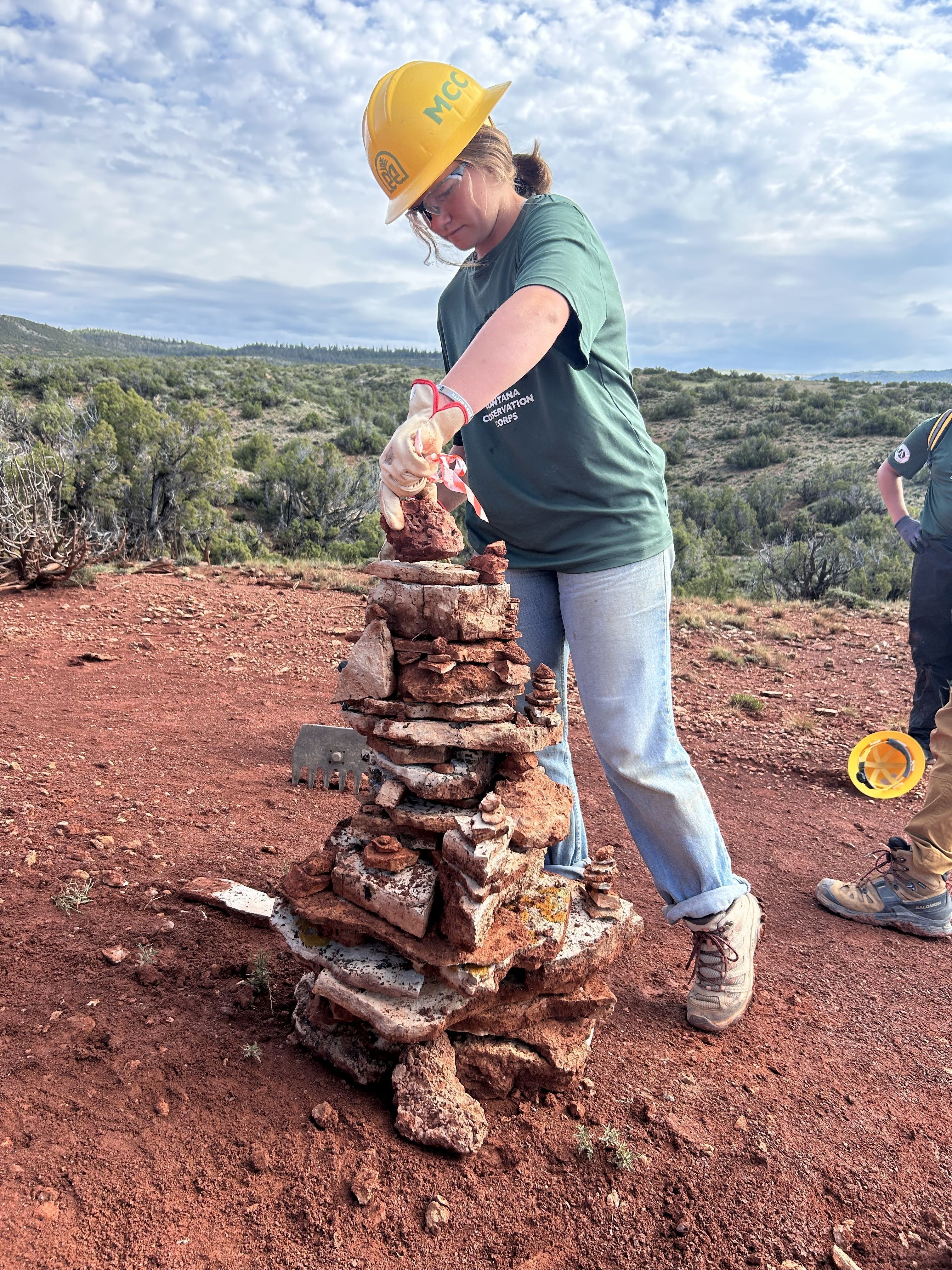 A youth crew member places a rock on top of a rock tower