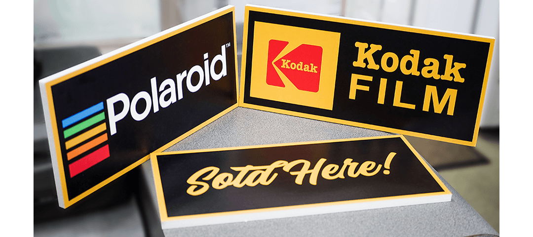 Signs printed on thick foam board with retro Polaroid and Kodak logos - Yellow script font reads "Sold Here!"