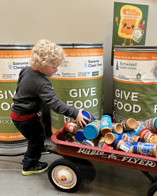 Young boy doing a food drive and holding up a sticker that says "i helped end hunger and so can you"