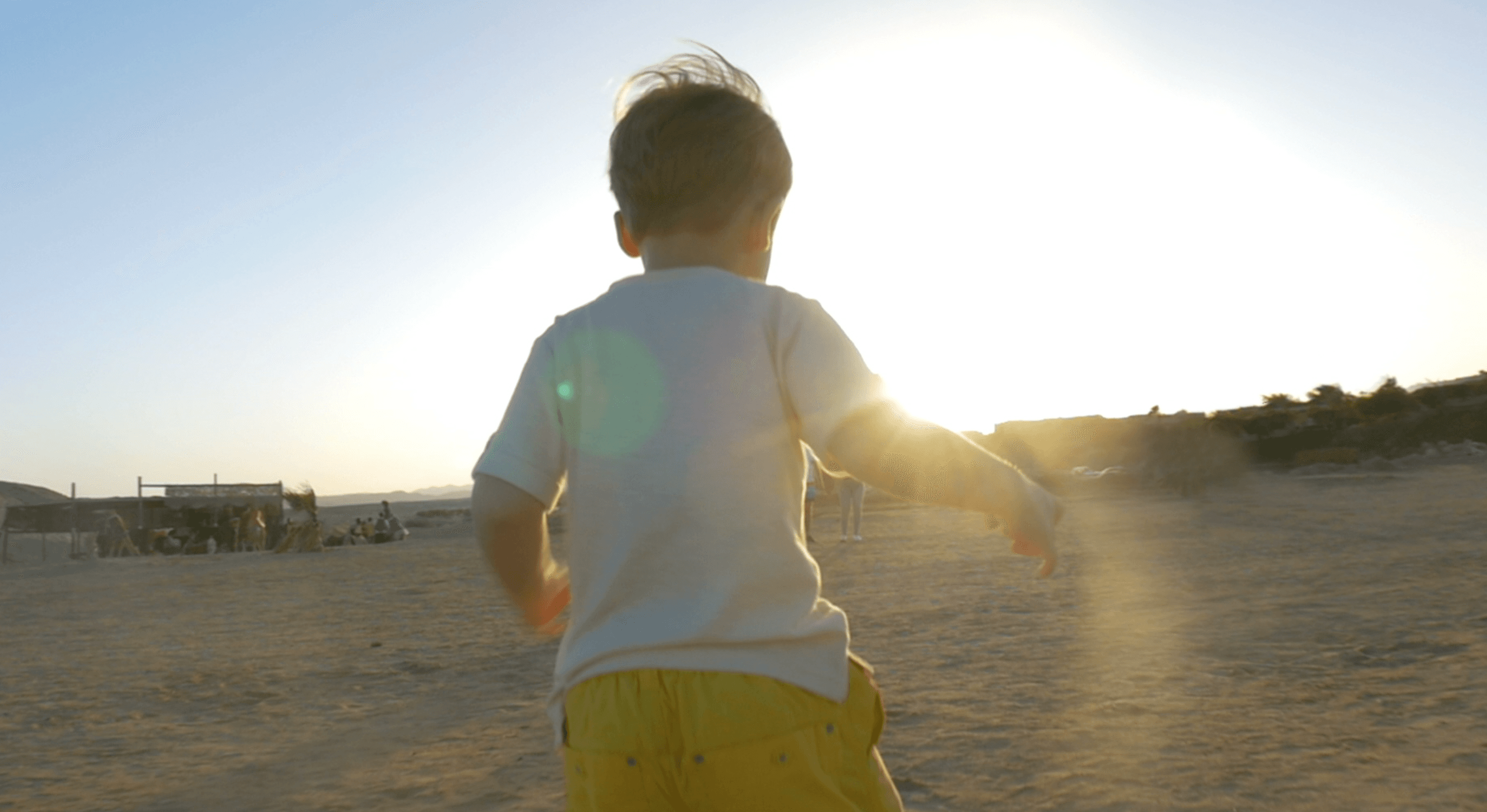 young boy facing away from the camera and running towards the sun