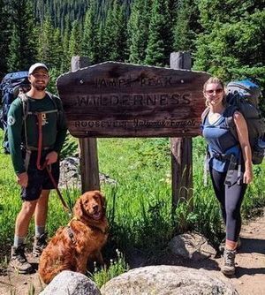Paul, wearing an MCC t-shirt, poses at the entrance of a trailhead with a woman and a golden retriever.