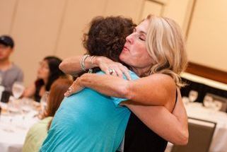 Two women embrace one another. The one facing the camera has her eyes closed.