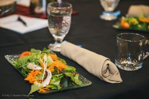 A green salad is placed on a black table cloth with rolled silverware next to the plate.