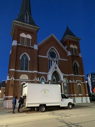 Two men stand together at the back of a large box truck parked in front of a church.