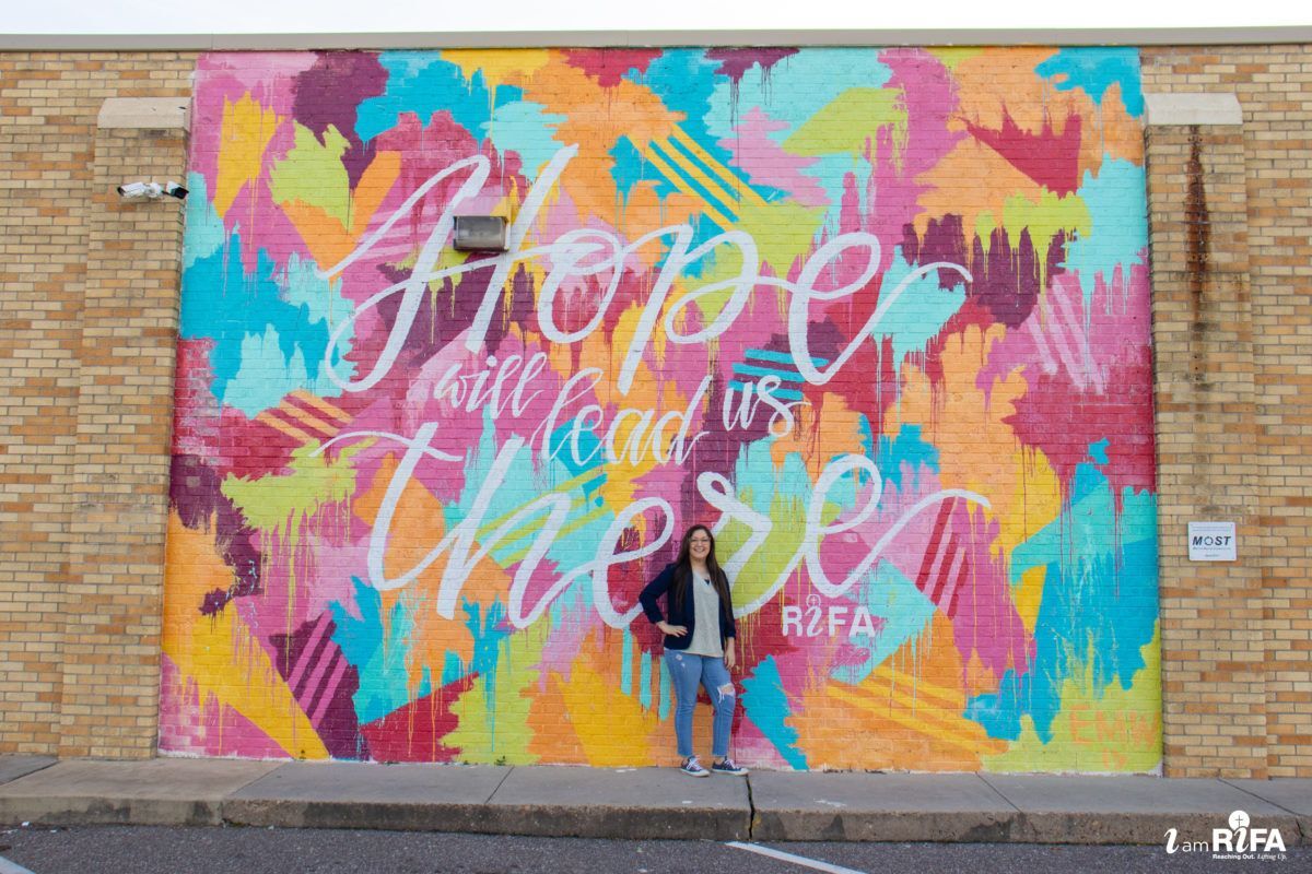 Woman standing in front of "Hope will lead us there" colorful wall mural