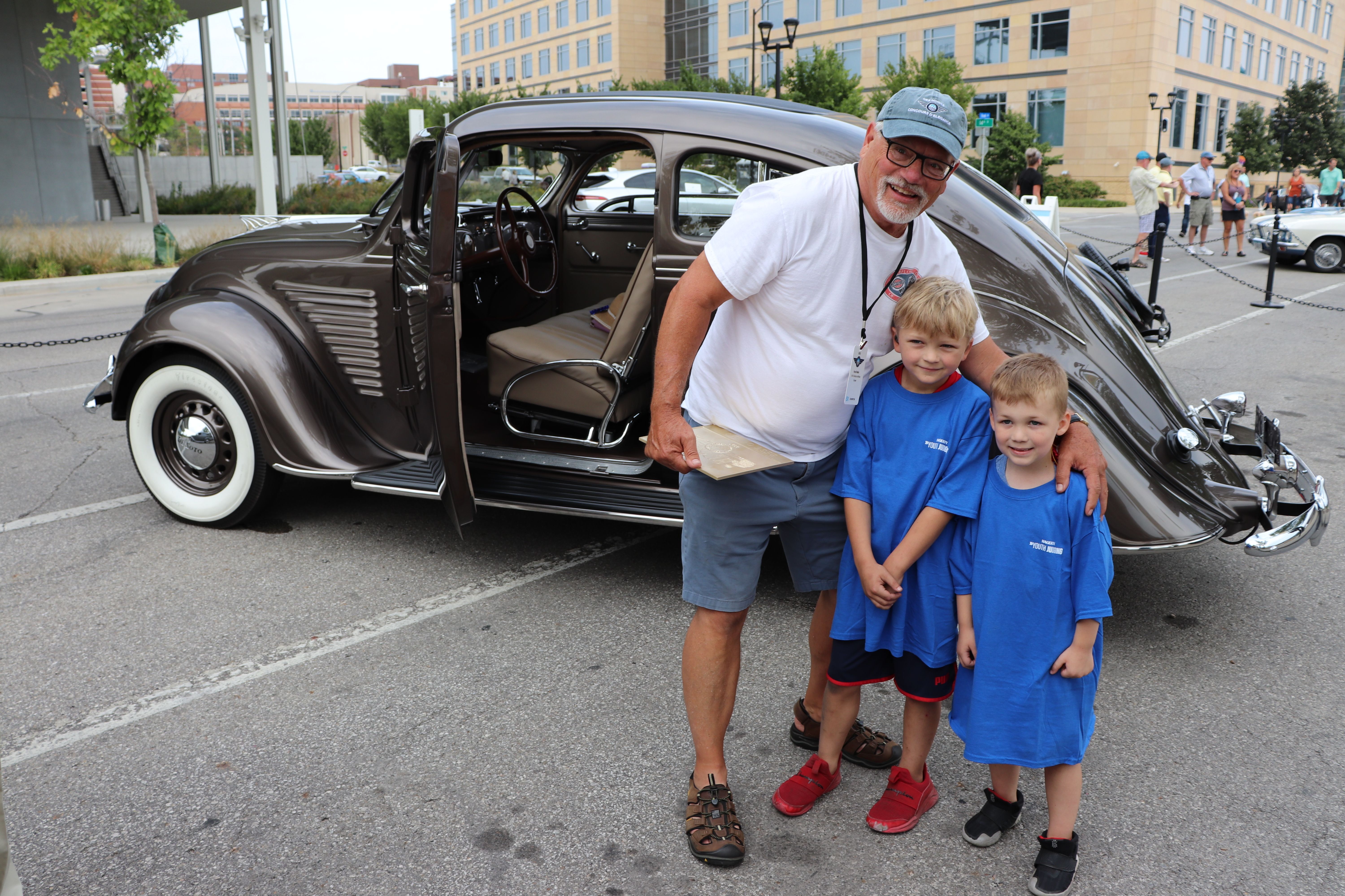 Two CCC kids standing with a classic car and its owner. 