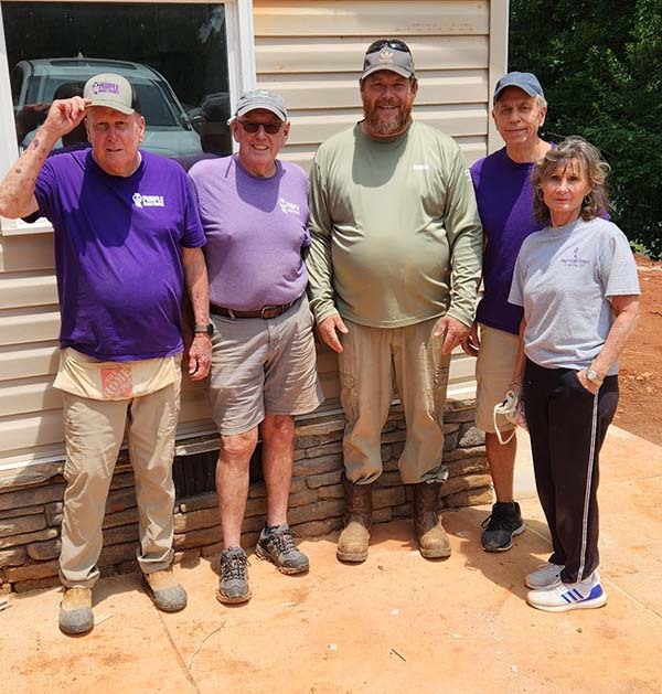 Two Purple Heart Homes volunteers in purple shirts working together on porch trim
