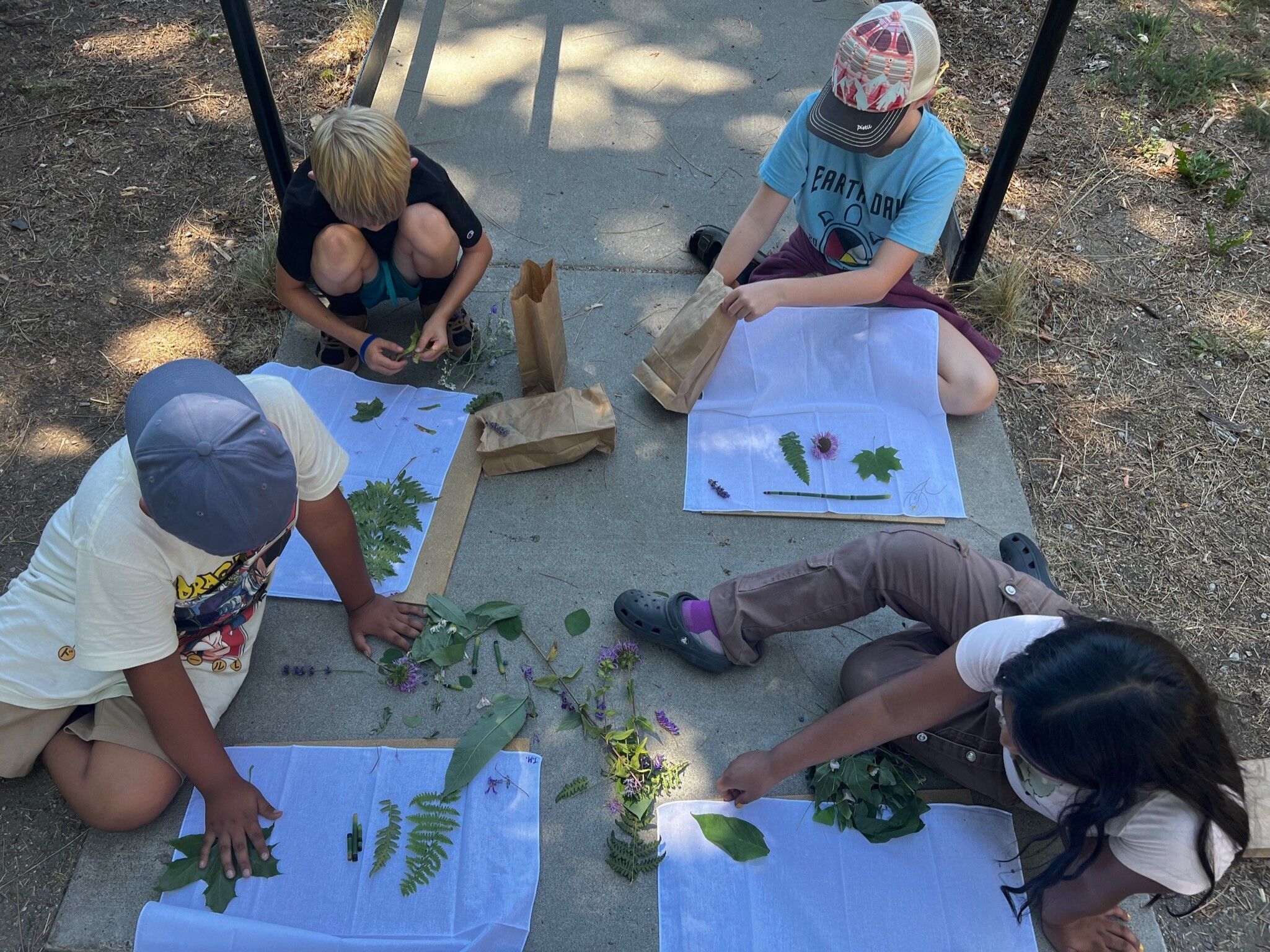 Wenatchee River Institute's Orondo After School Program Summer Camp children doing a nature craft outside on the sidewalk with leaves.