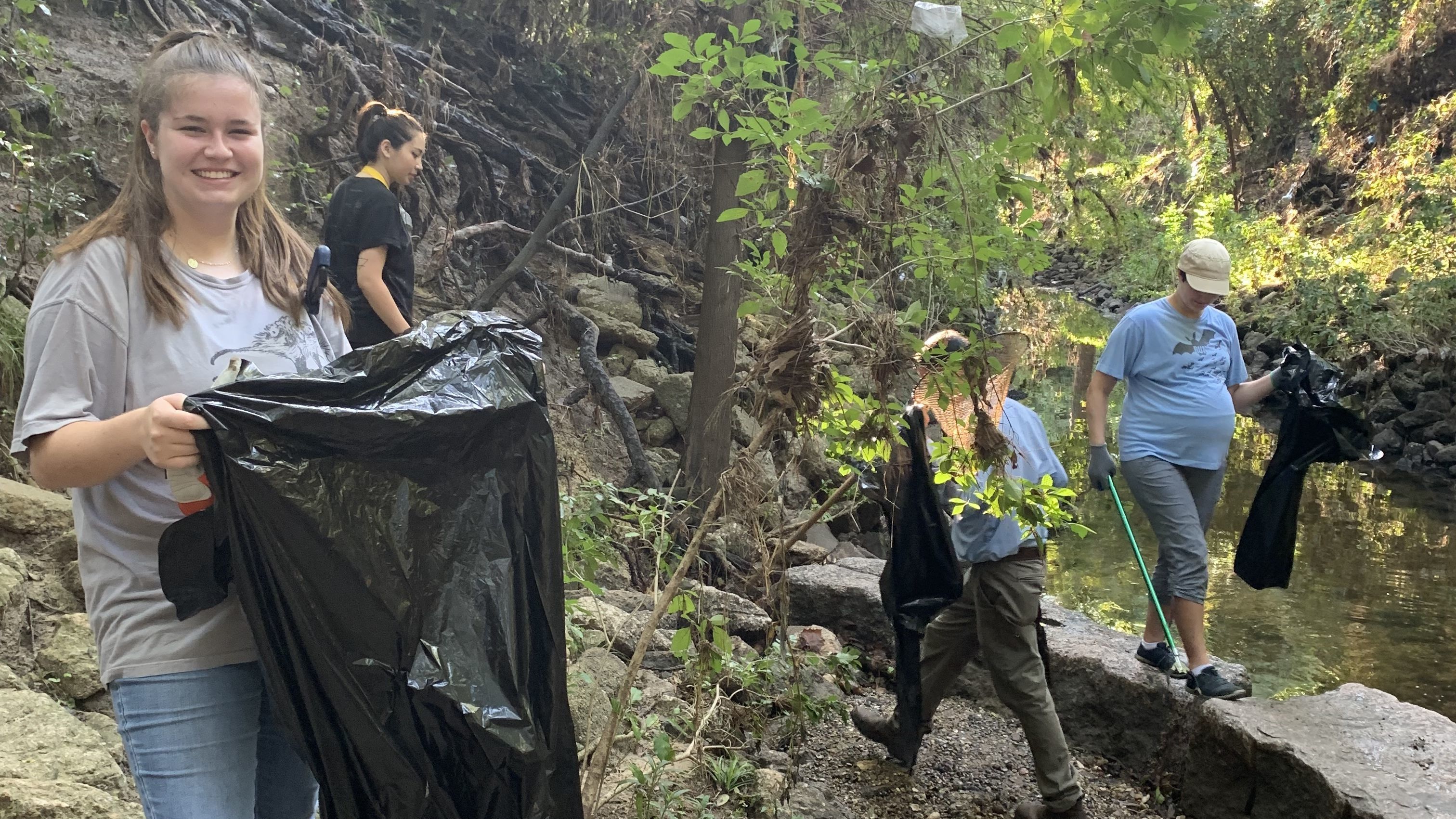 Volunteers smiling and cleaning up litter on the stream bank