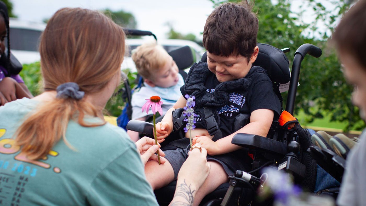 Paraprofessional and young boy in wheelchair looking at flowers outside