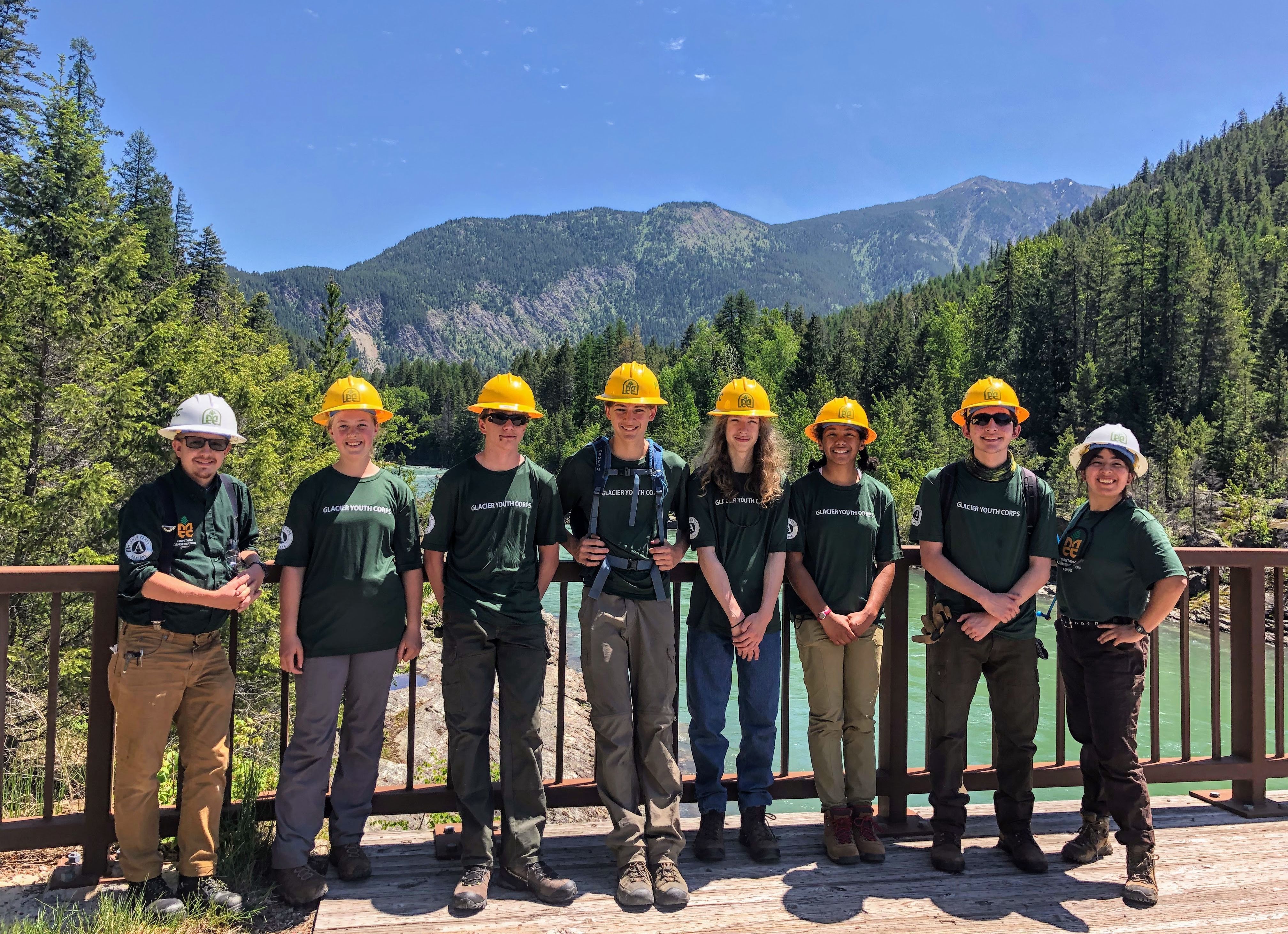[Image Description: Six Youth MCC members and their two leaders are standing together on a bridge. In the background, dark green trees cover the mountains and the water below them is a bright, turquoise color.]
