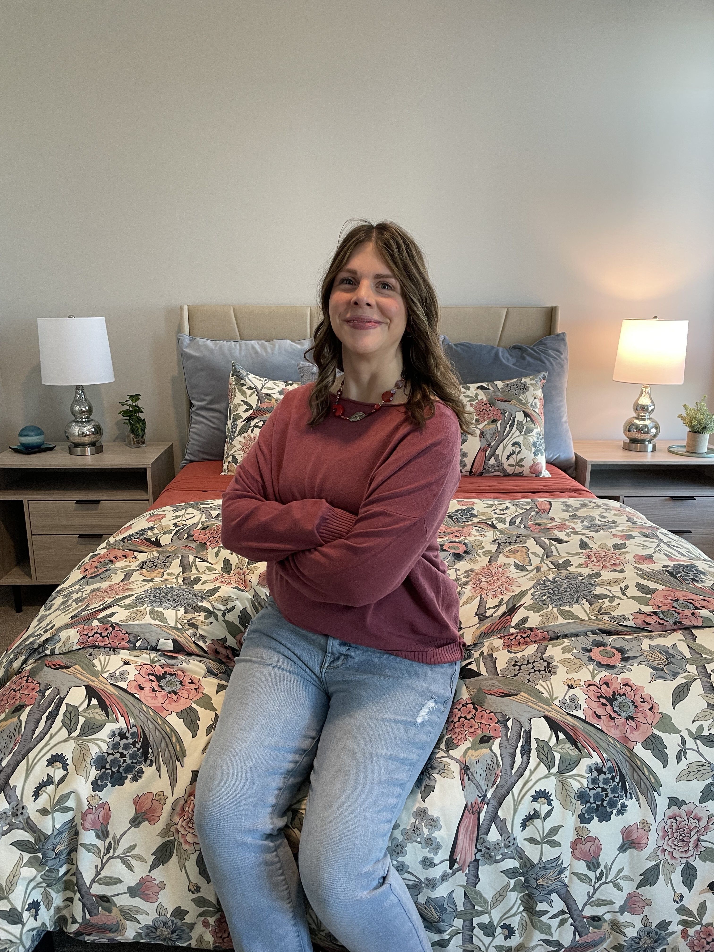 Brianna sitting proudly on a bed in her new apartment, arms crossed in front of her with a big smile 