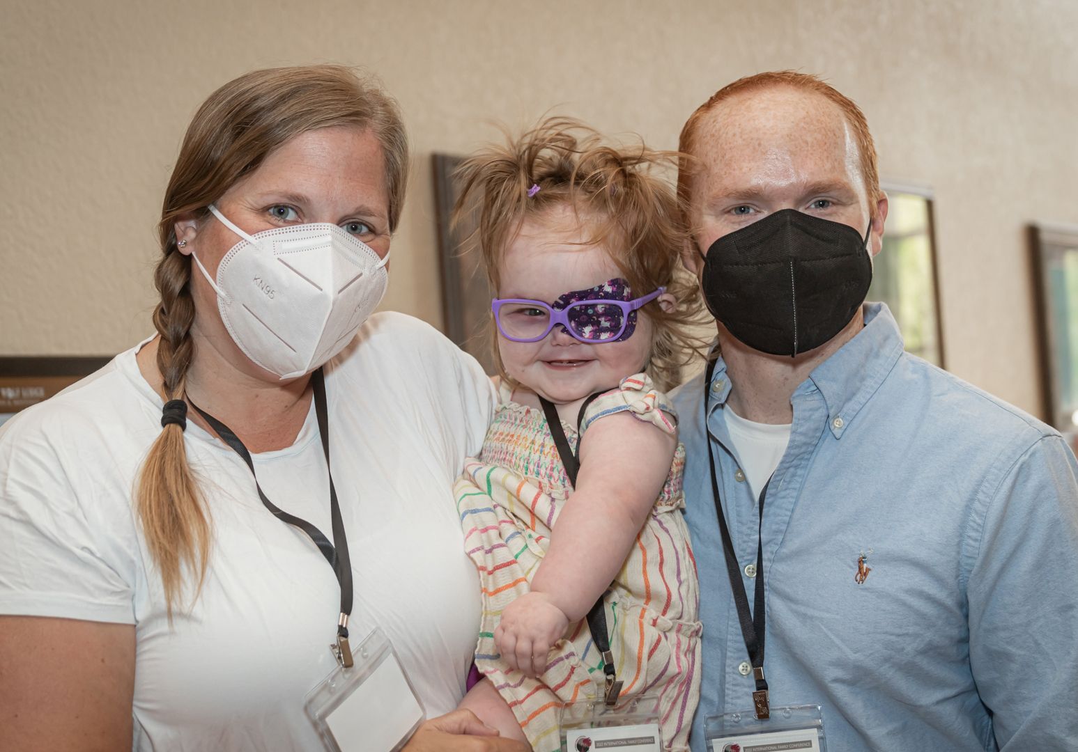 Family of three, mom on the left, daughter in the middle, and dad on the right. All wearing face masks. Little girl in the middle is wearing an eye patch.