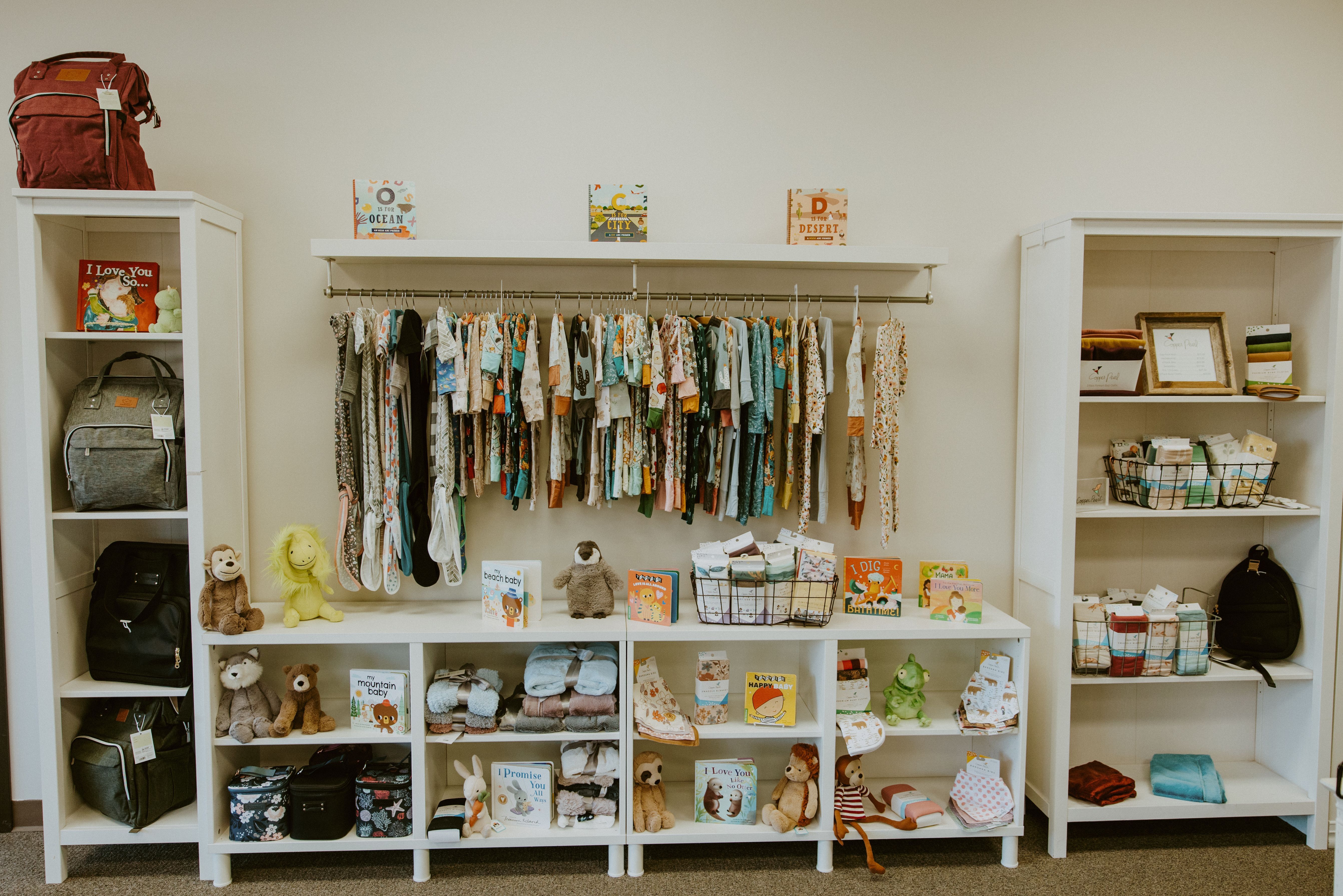 Image of white retail shelving with infant clothing, books, blankets, and pump bags organized on it.