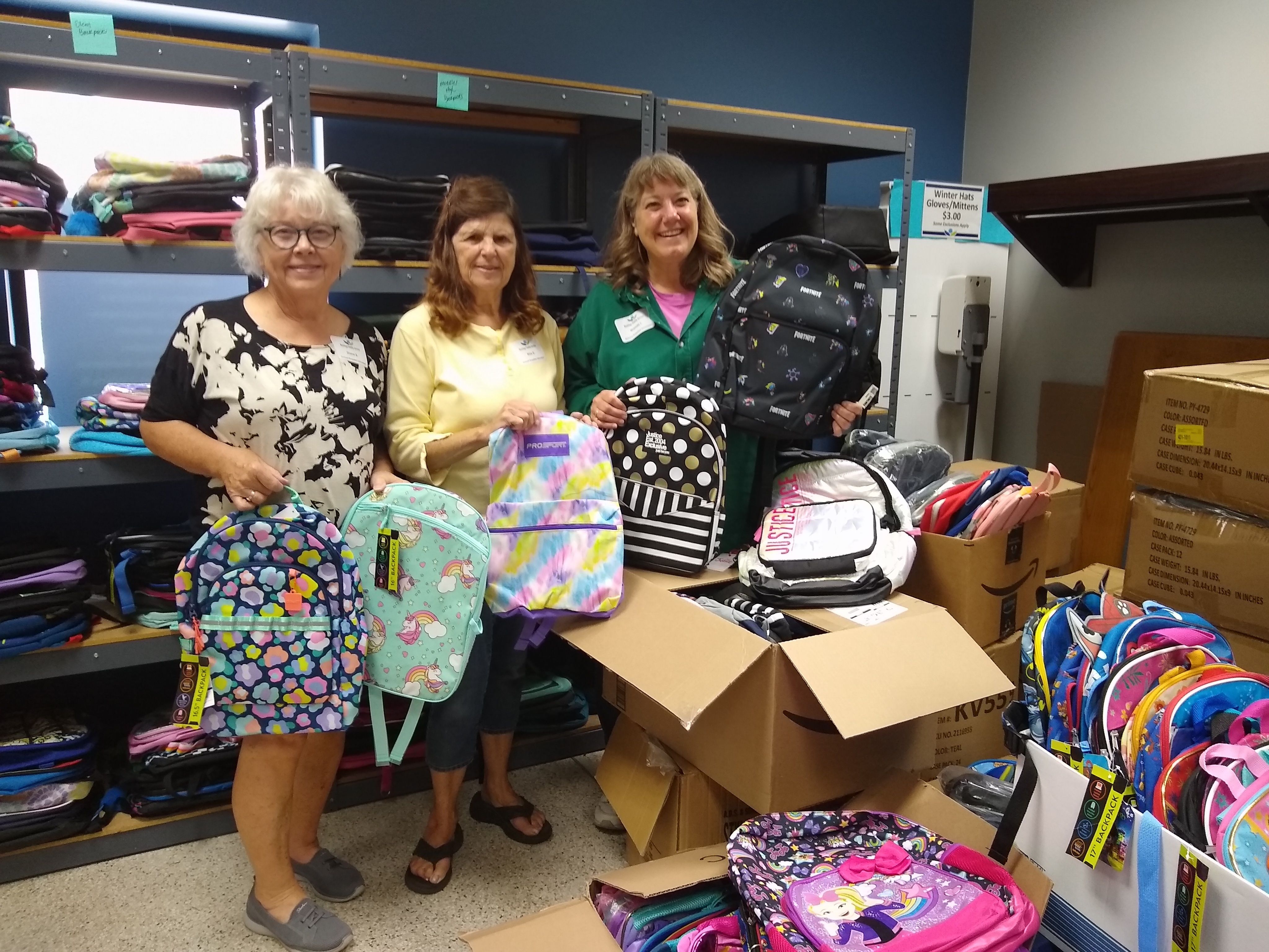 Three volunteers sorting backpacks in the school supplies room at Hastings Family Service.