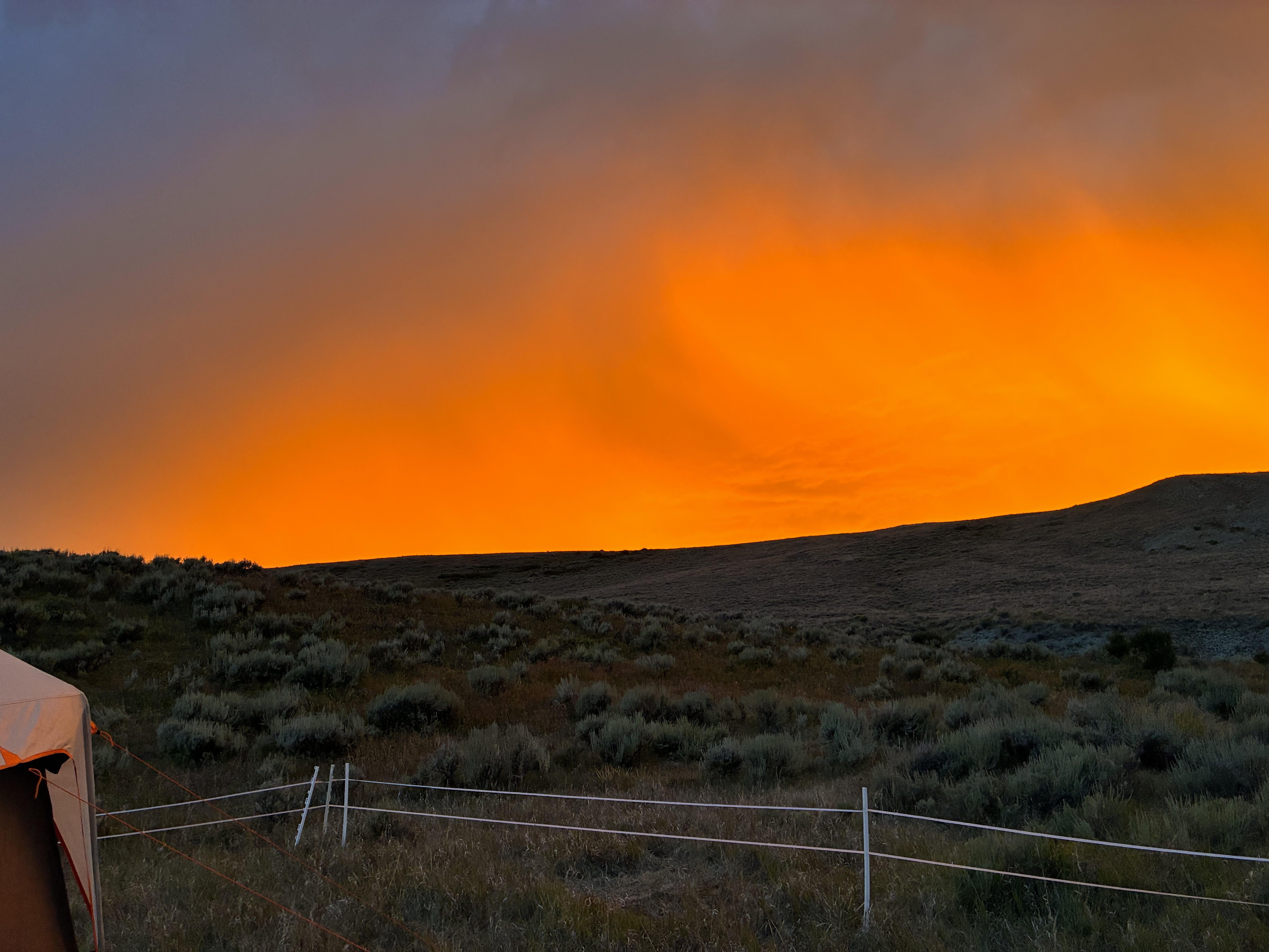An orange sunset in the sky above some sagebrush covered hills