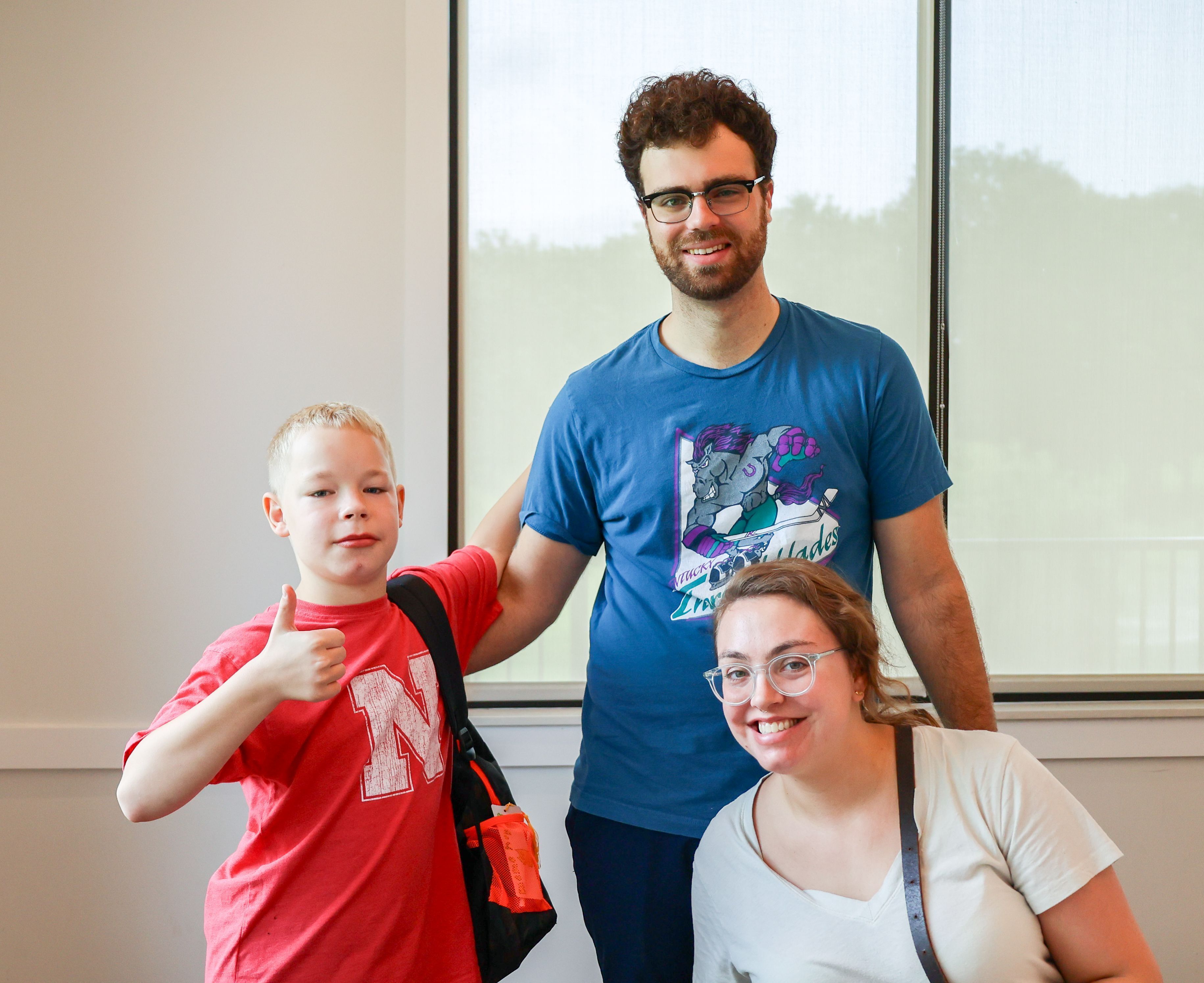A Big Couple and their Little from Big Brothers Big Sisters of the Midlands smile together indoors; the Little gives a thumbs-up while standing beside his mentors, showing their positive connection and friendship.