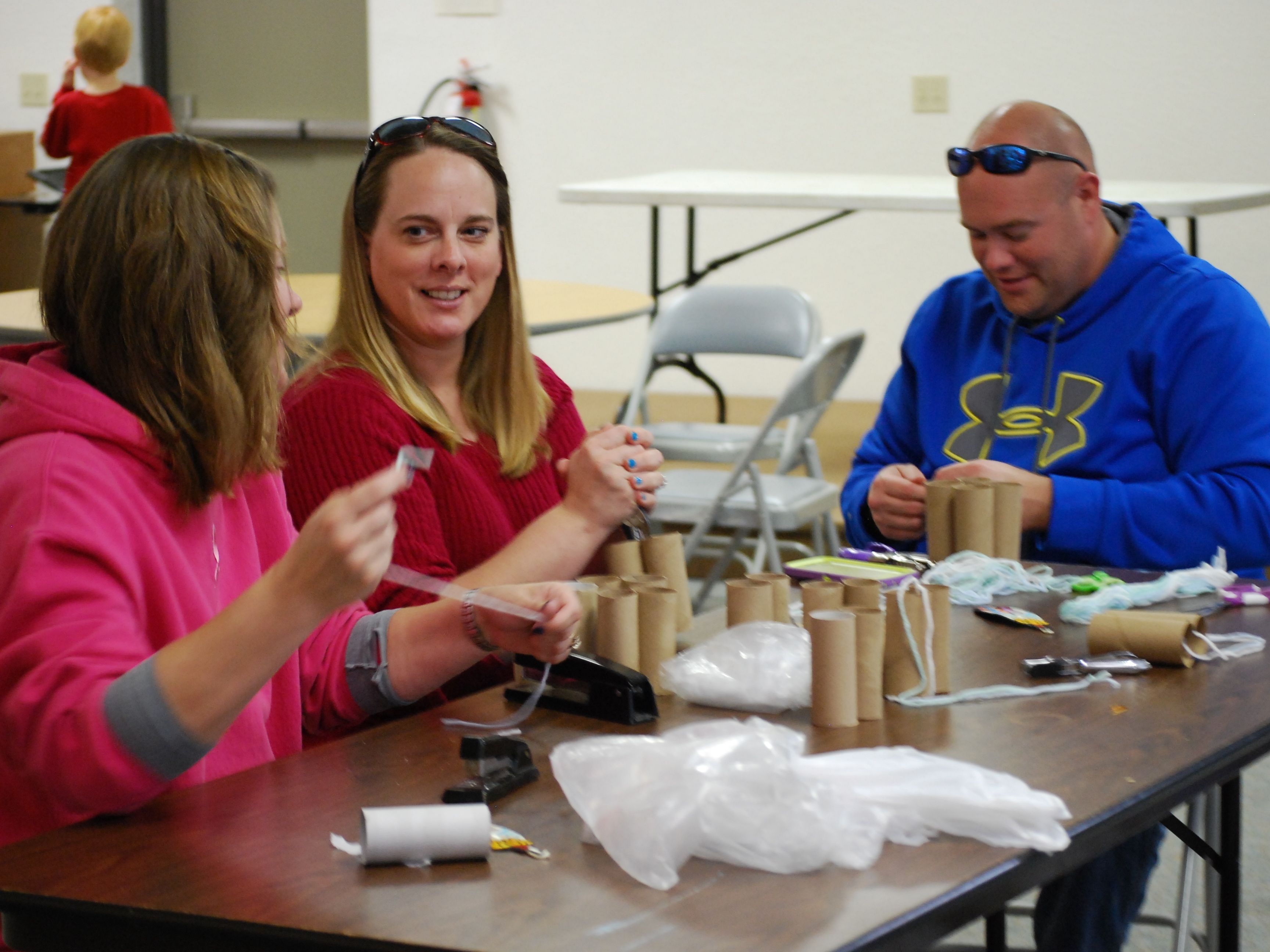 Three volunteers are shown construction toilet paper binocular for first graders to use during their field trips. 
