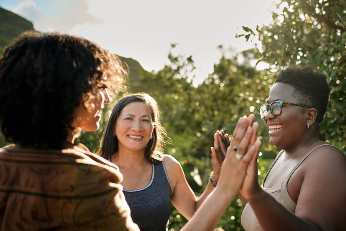 Three women outside touching hands together
