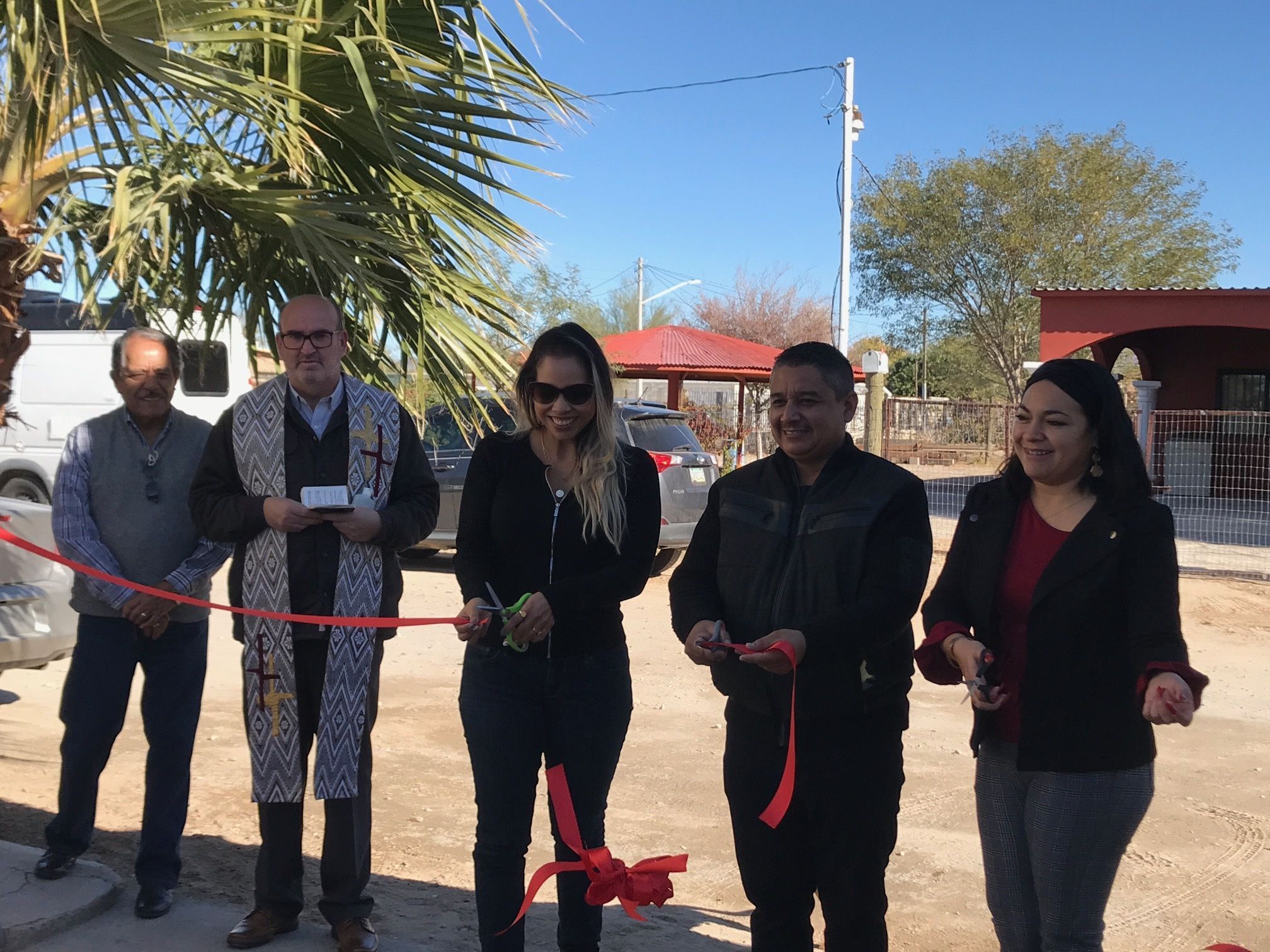 Red ribbon with a bow in front of a gathering in a courtyard under a clear blue sky.