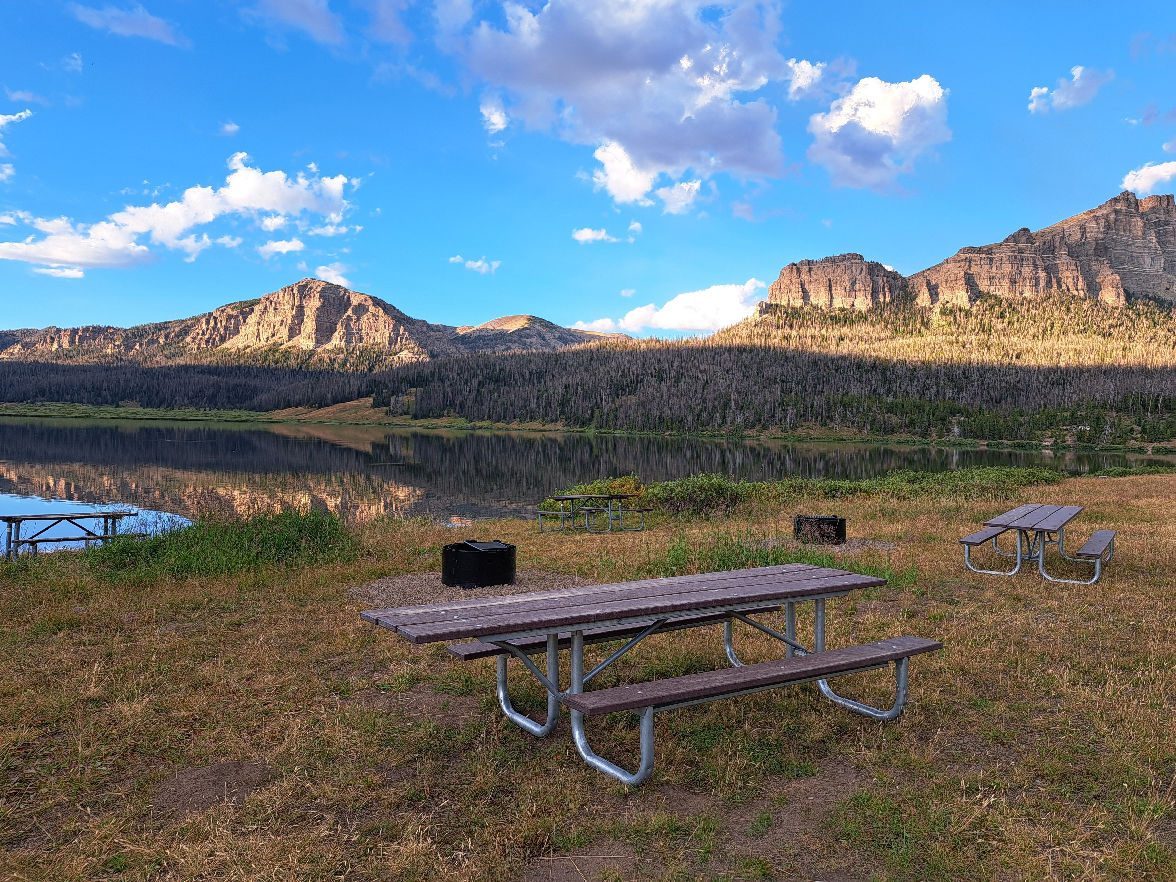 A view of a picnic table next to a lake, with mountain cliffs in the background.