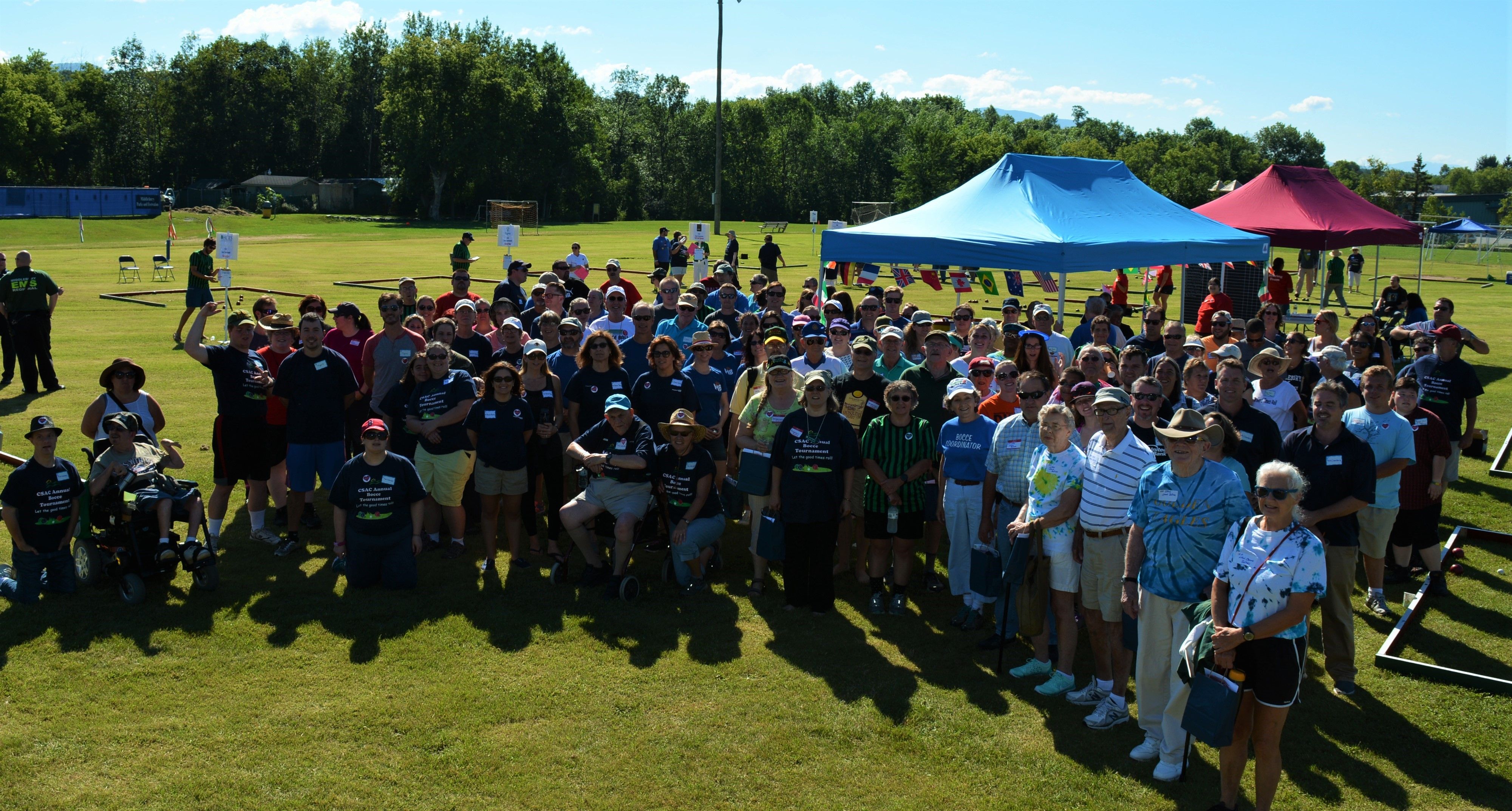 Bocce group photo of players and volunteers sitting, standing, and kneeling, on the field together from CSAC's Bocce tournament.