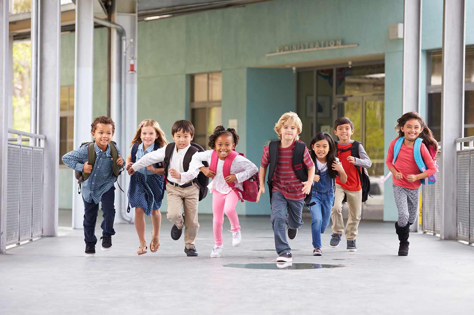 Young school children running in the hallways wearing backpacks.