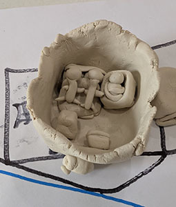 Clay house sculpture with roof removed, showing clay family figures inside