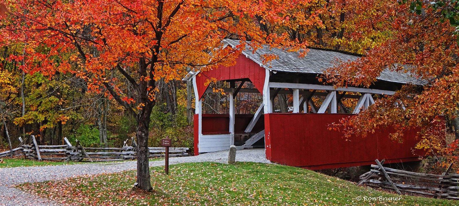 Red and white covered bridge in autumn with colored leaves.