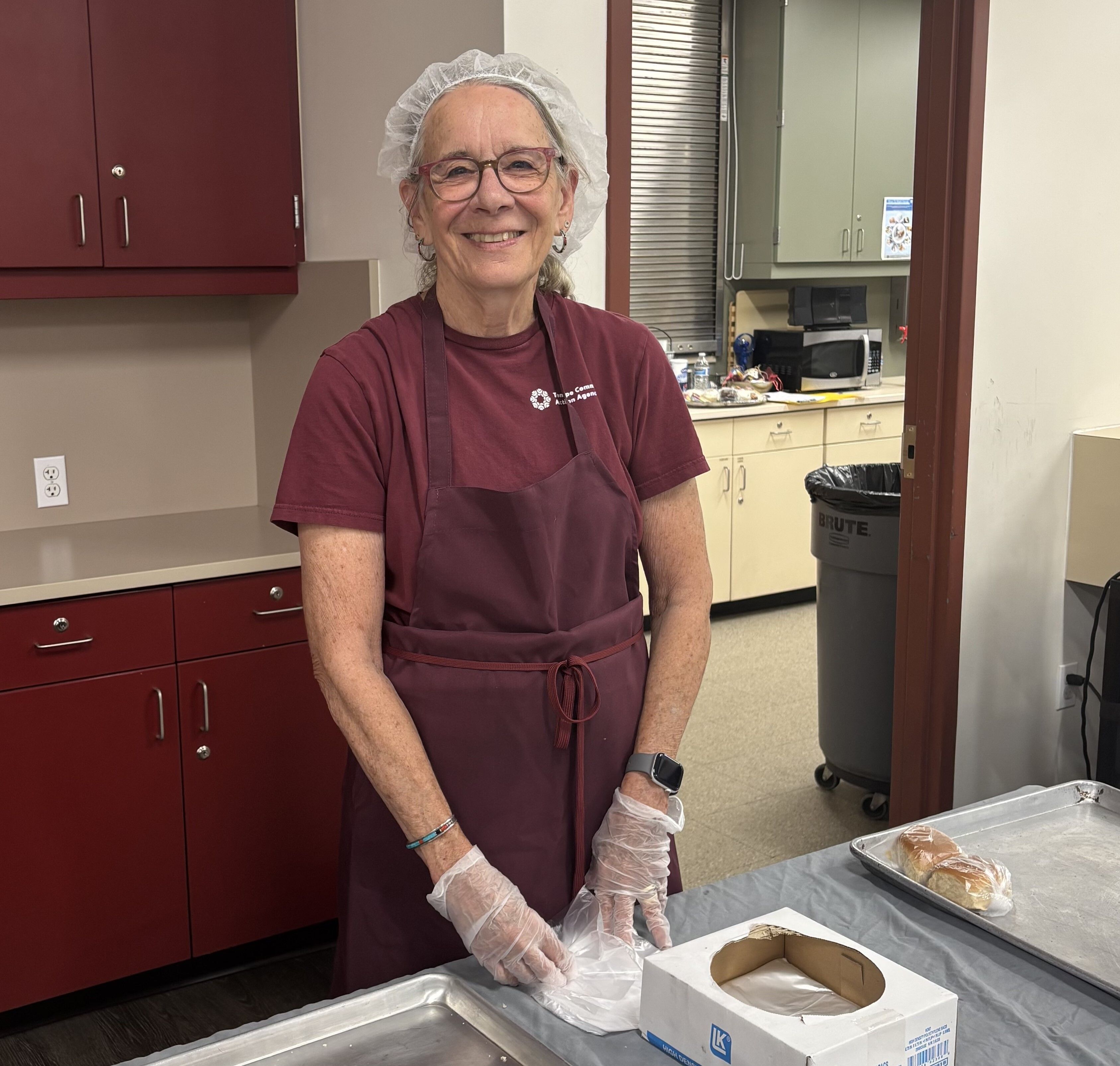 Linda is in a maroon shirt with hair net and gloves on.