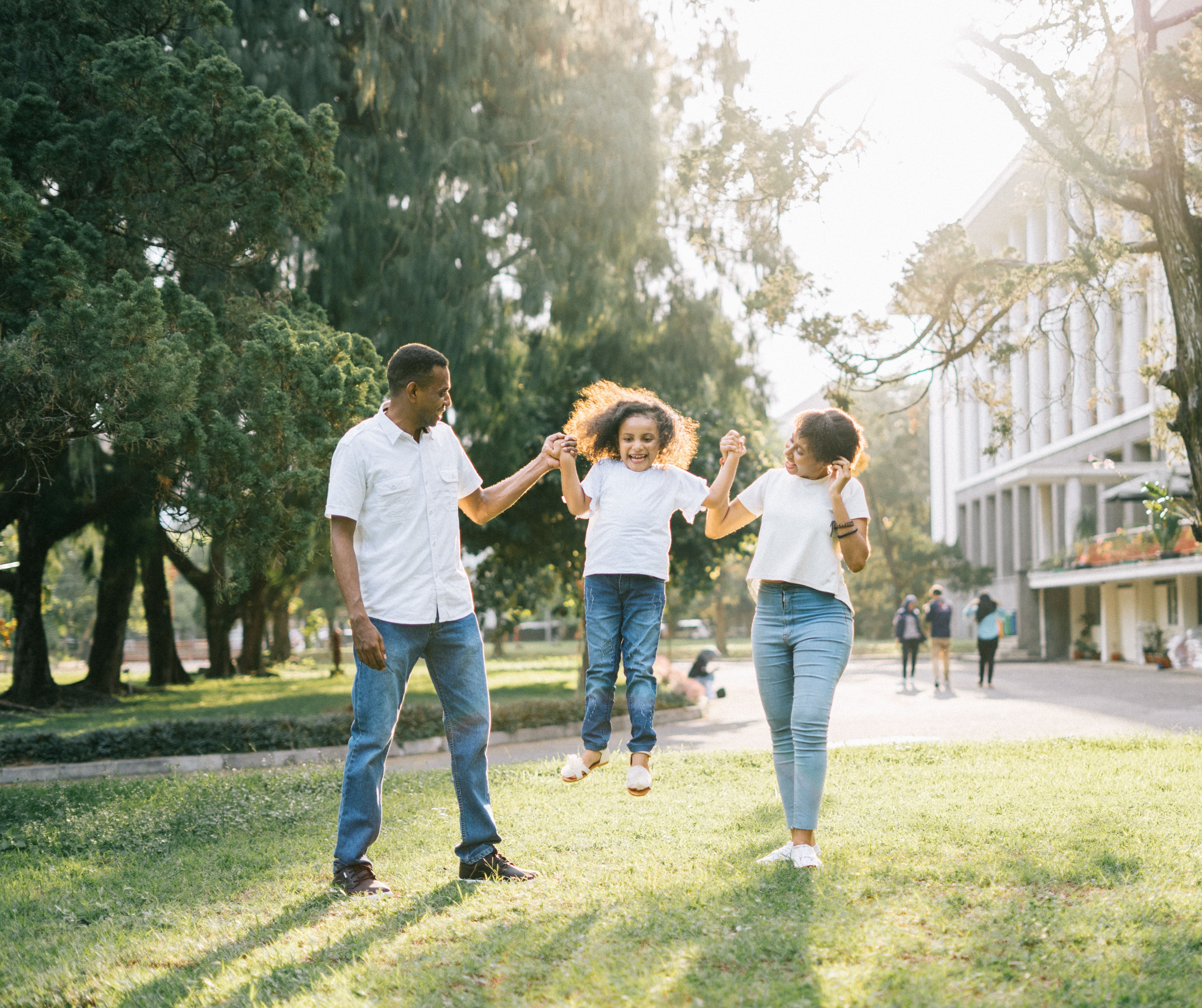 Parents hold hand with young child while walking outdoors on college campus