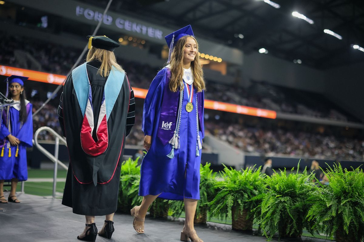 Hebron High School student in a blue cap and gown and purple LEF stole walks across the stage at graduation.