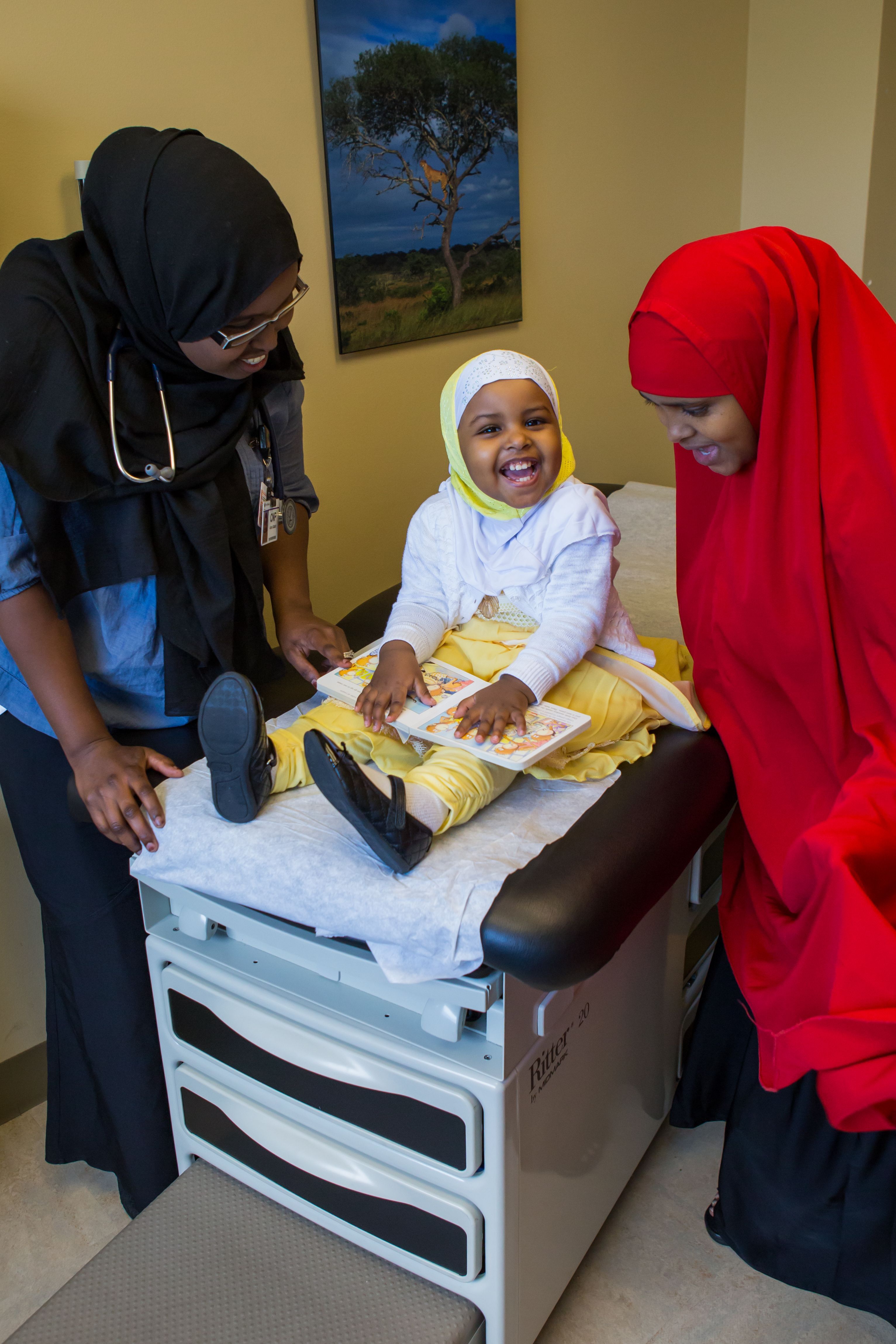 Mother, toddler daughter, and clinician smile with book together